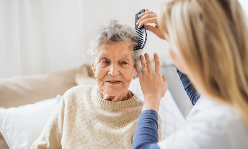 Vermittelte Pflegekraft kämmt Dame die Haare